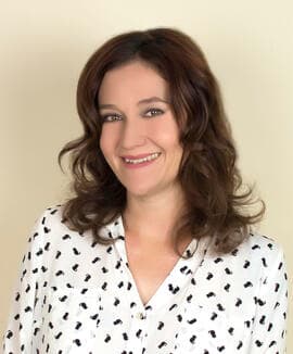 Melissa Hall smiling for the camera in a white shirt with a cat pattern on the shirt.