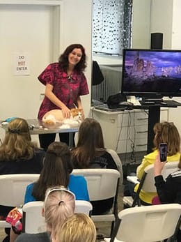 Melissa Hall demonstrates grooming on an orange tabby cat in front of an audience of seated students.